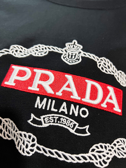 プラダ 胸に麻縄の刺繍がされた、クラシックな1986のスローガン文字ロゴ半袖Tシャツ